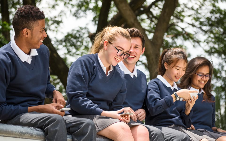 Secondary school students laughing together over their phones